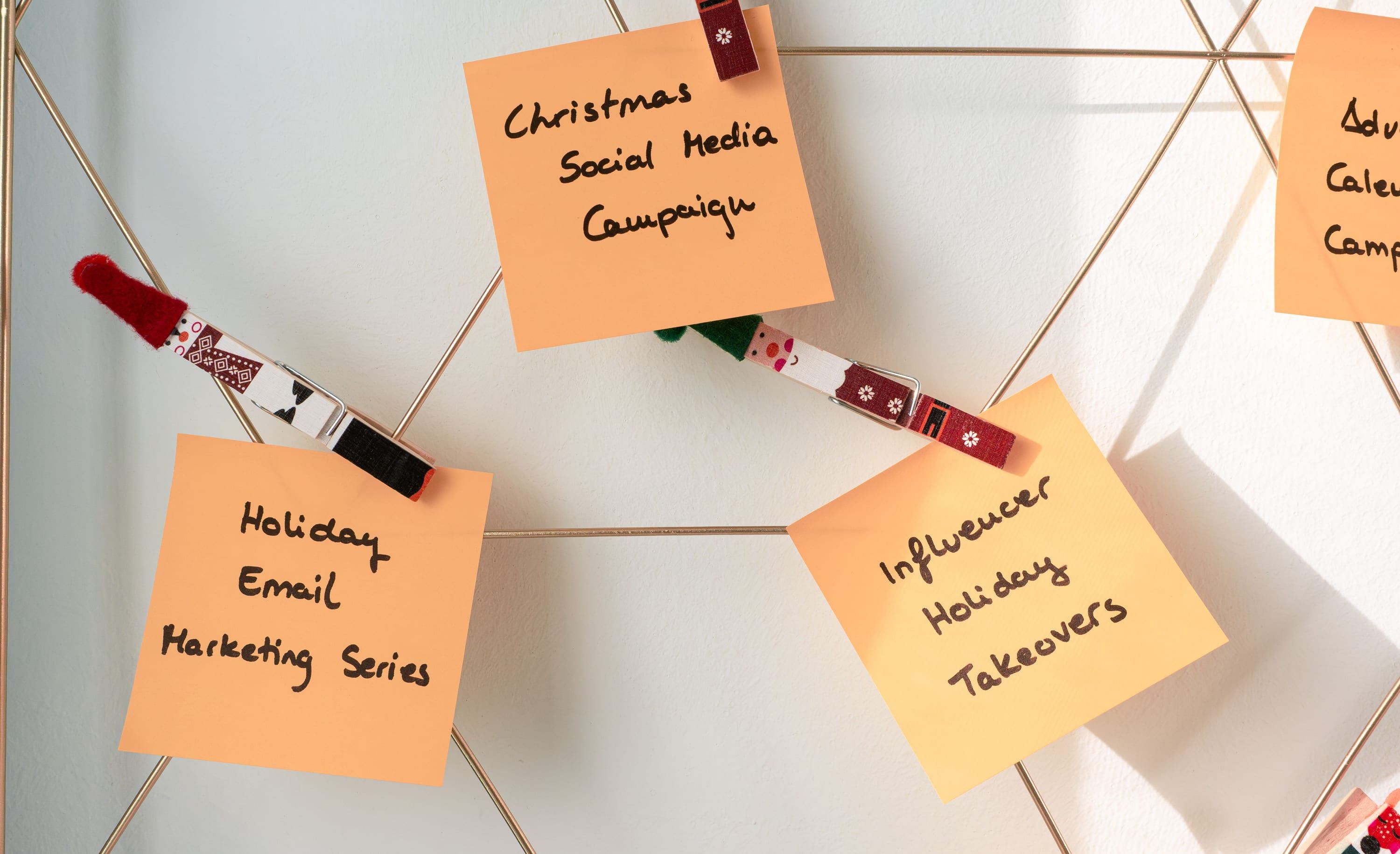 Orange sticky notes pegged to wire on a white wall, each carrying a handwritten campaign name.