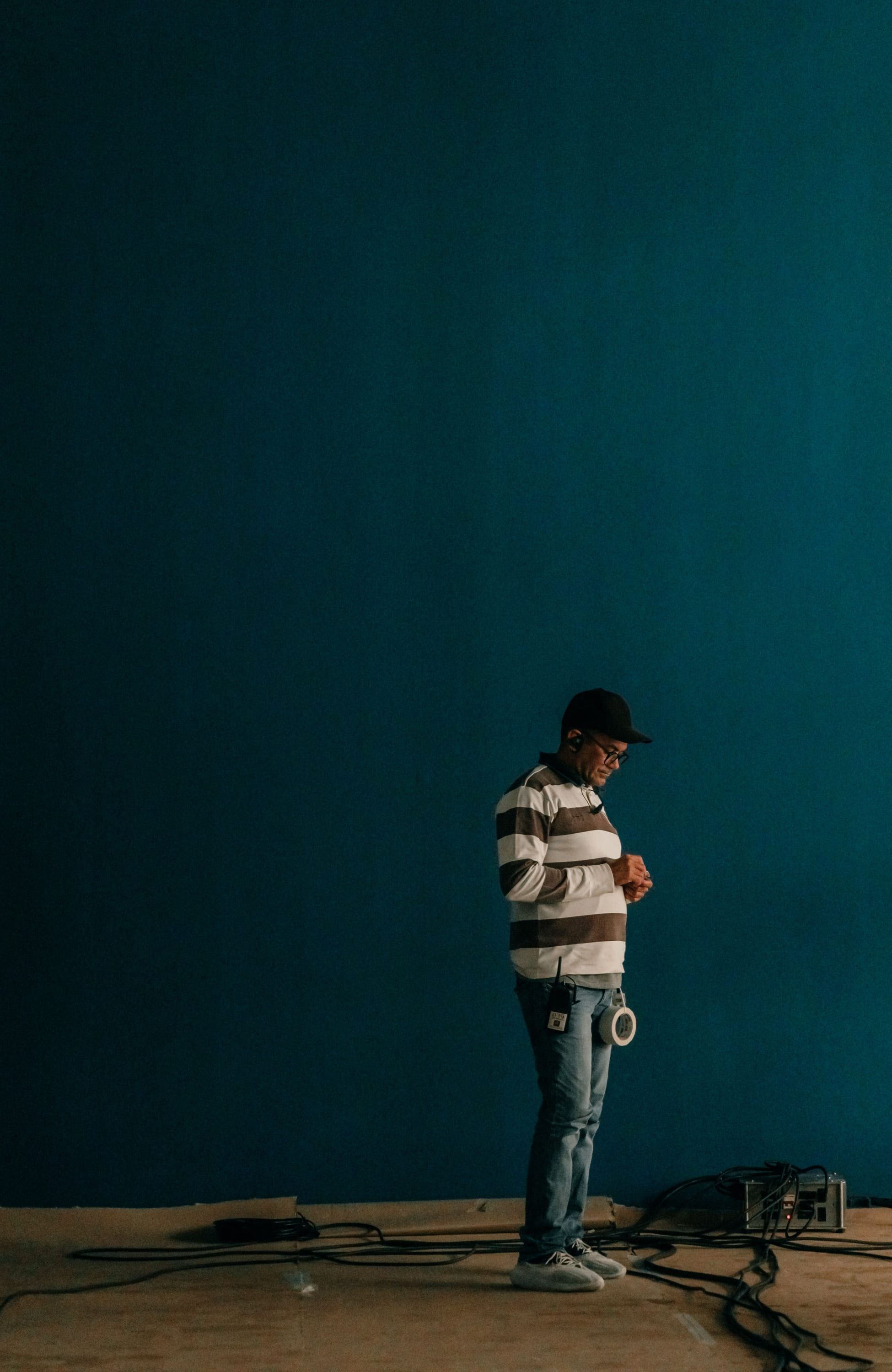 A person standing alone against a large deep teal wall, cables running across the floor at their feet.