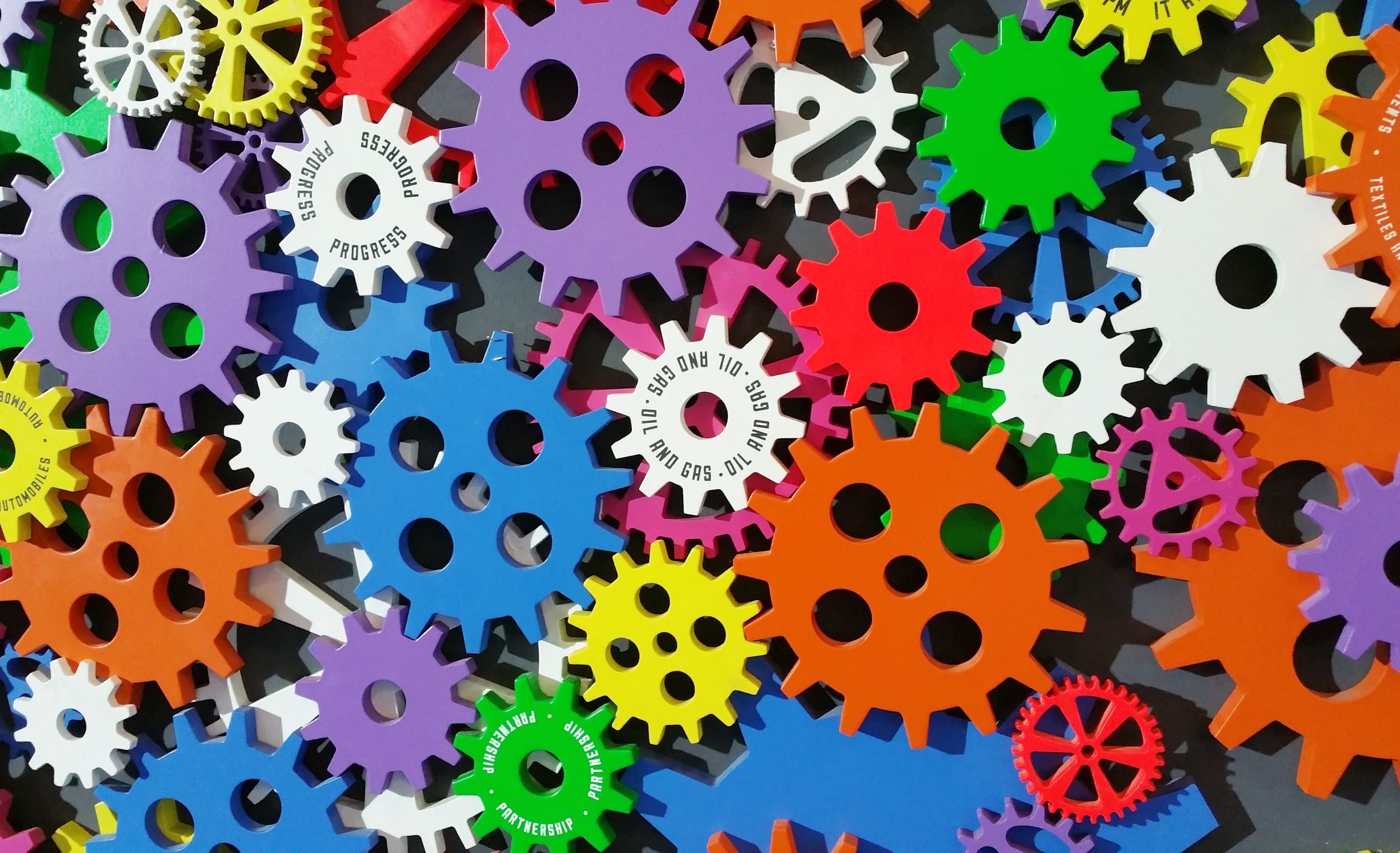 Dozens of brightly coloured plastic cogs of different sizes laid flat and interlocking.