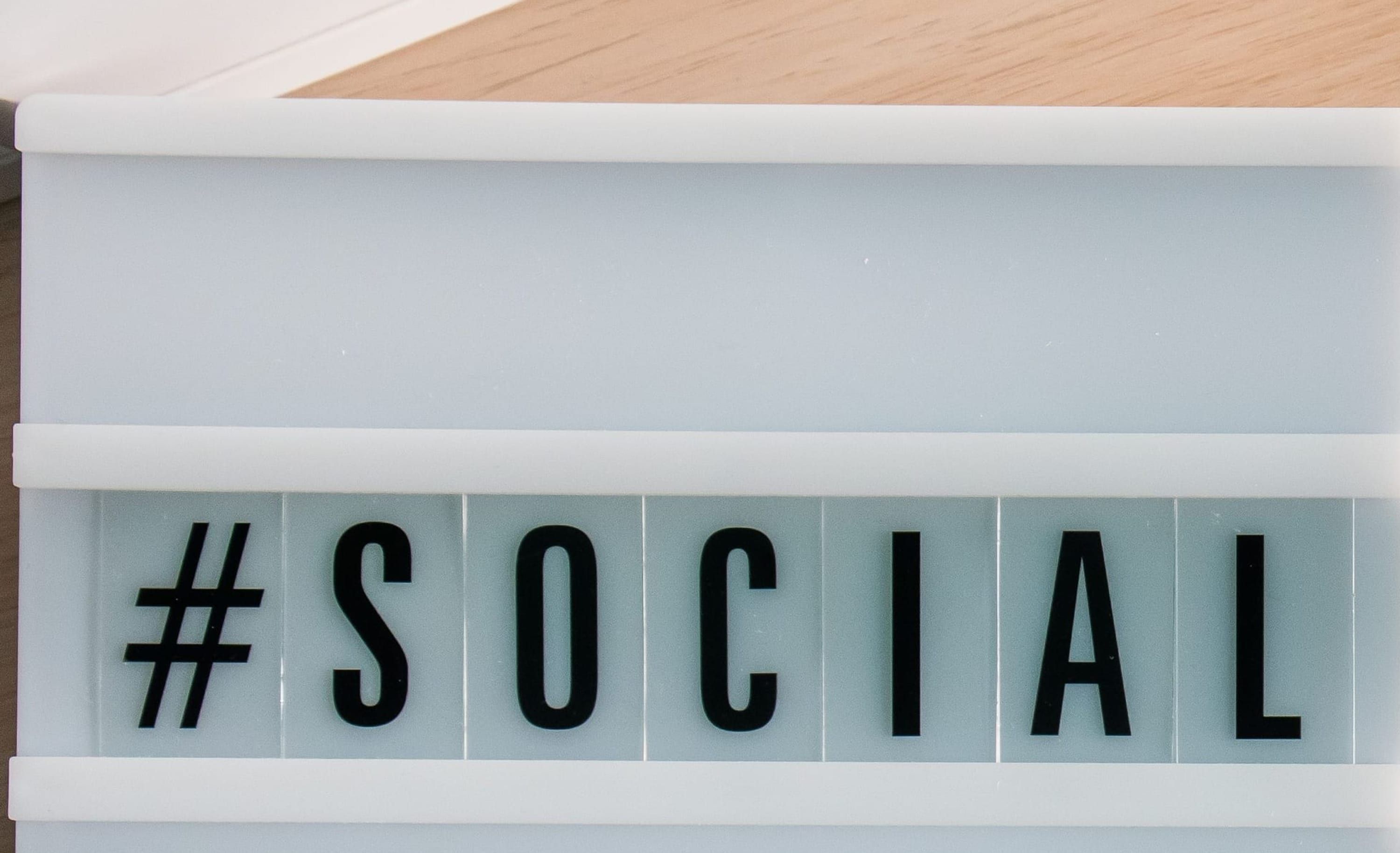 A white letterboard reading hash SOCIAL, filling the frame against a light wooden desk.