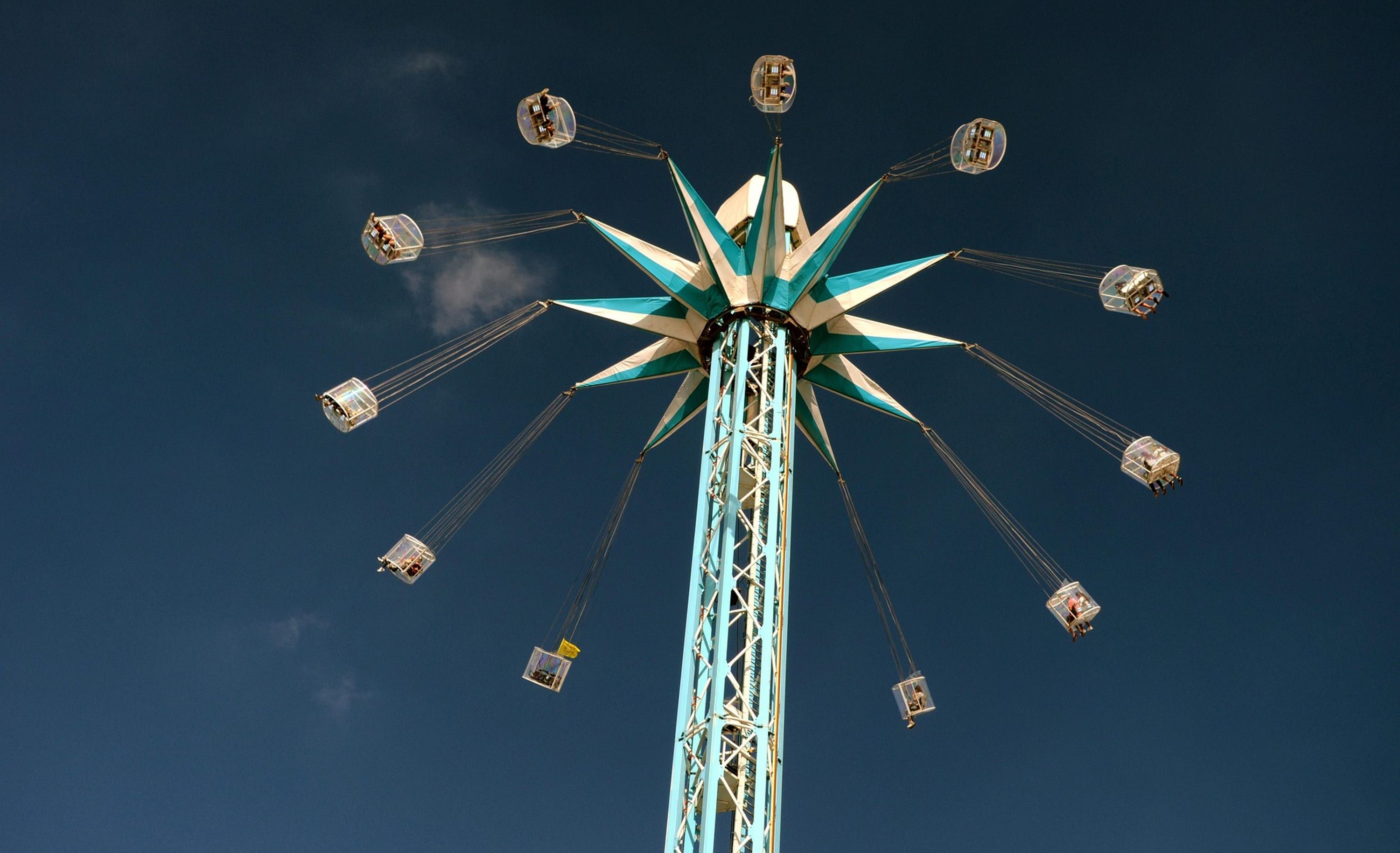 A fairground swing tower shot from directly beneath, its arms radiating against a deep blue sky.