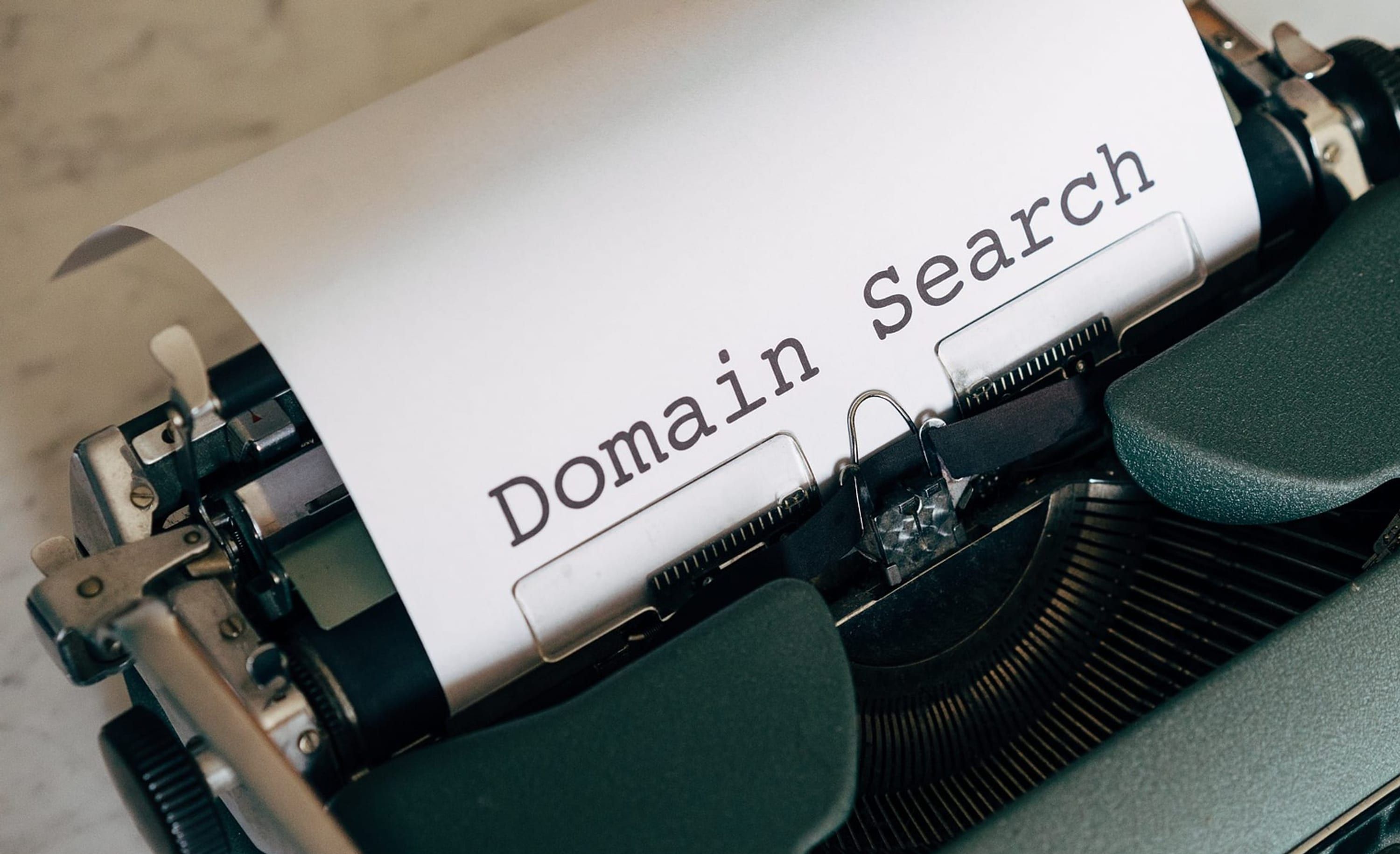 A green mechanical typewriter with a sheet in the roller reading Domain Search.